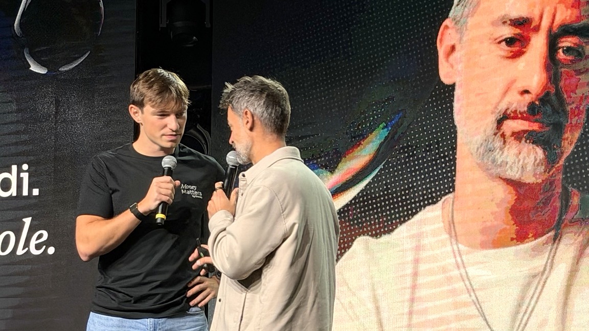 Due ospiti conversano sul palco di Money Matters davanti a un maxi schermo.